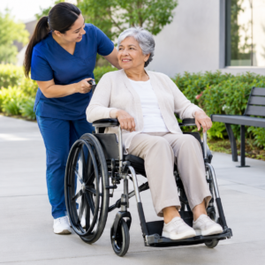 Caregiver practicing safe wheelchair use with an older adult on level pavement
